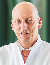Portrait von Chefarzt Professor Karl-Dieter Heller vor einem grünen Hintergrund. Er blickt freundlich in die Kamera.
