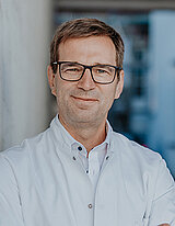 Portrait von Chefarzt Dr. Hinrich Köhler vor einem blauen Hintergrund. Er blickt freundlich in die Kamera.